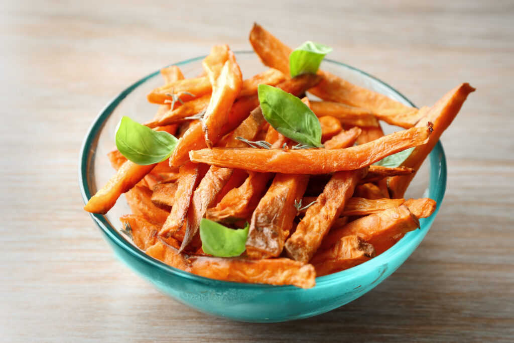 Glass bowl with deep fried sweet potato on wooden background